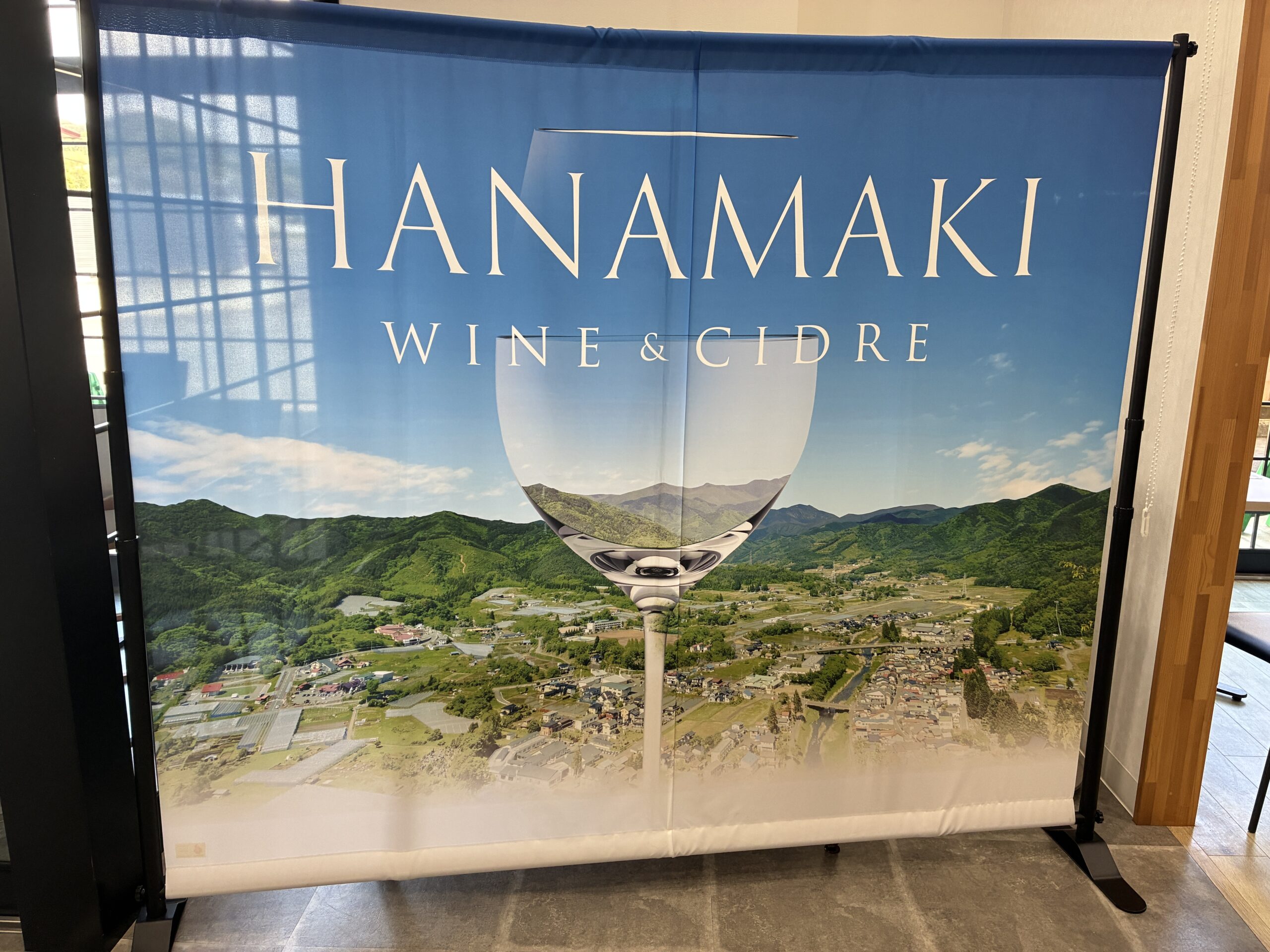 HANAMAKI WINE & CIDREのバナー。花巻市の緑豊かな景観とワイングラスが合成された印象的なビジュアル